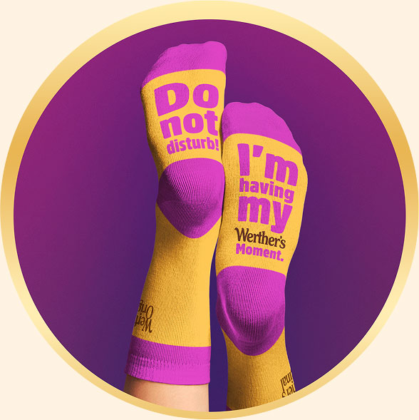 Gelbe Socken mit Werther's Logo, lila Details und auffälligem Spruch auf der Fußsohle: „Do not disturb! I’m having my Werther’s Moment“.